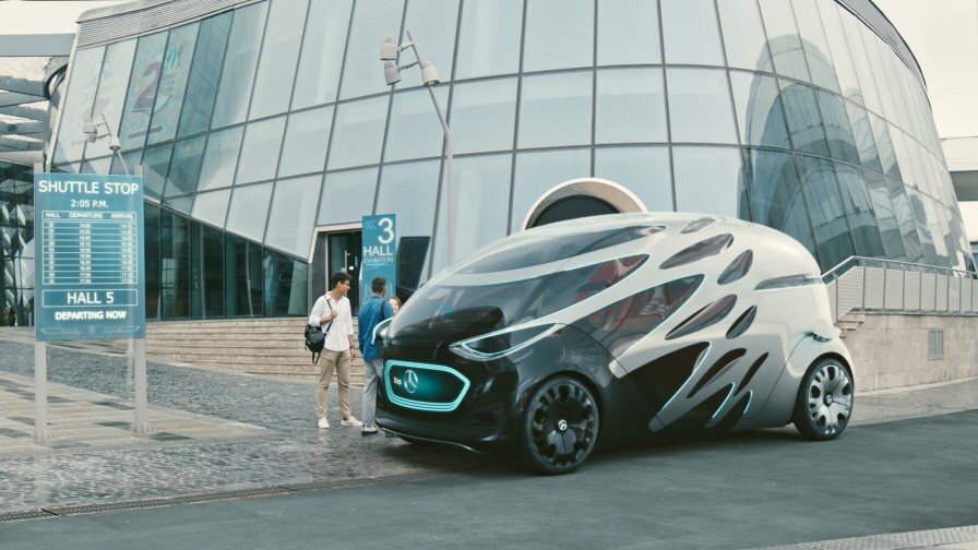 Un vehículo autónomo futurista estacionado en una parada de transporte frente a un moderno edificio de cristal, con dos personas paradas cerca conversando.