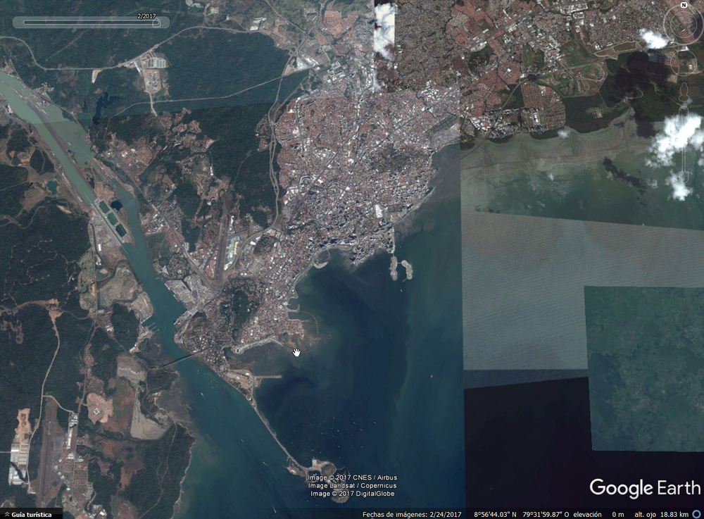 Imagen de satélite de una ciudad costera con densas zonas urbanas divididas por un río que desemboca en una gran bahía.