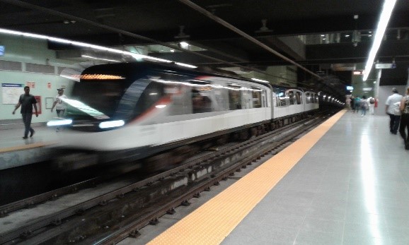 Un tren moderno que llega al andén de una estación de metro con pasajeros esperando y un efecto de movimiento borroso.