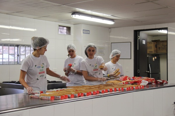 Cuatro mujeres con redecilla y camisetas blancas trabajando en una línea de envasado de alimentos en un ambiente de cocina blanco y limpio.