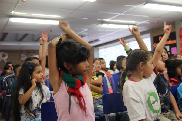 Niños levantando la mano con entusiasmo en un salón de clases.