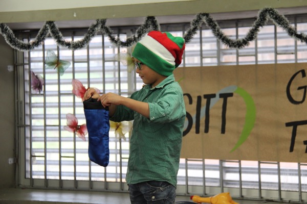 Un niño con un sombrero de elfo a rayas mira una media azul en sus manos en un evento festivo, con decoraciones en el fondo.