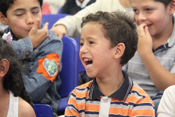 Un niño con una camisa a rayas se ríe alegremente entre otros niños en un salón de clases.