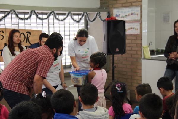 Un grupo de adultos distribuyendo material a los niños en un aula decorada con guirnaldas.