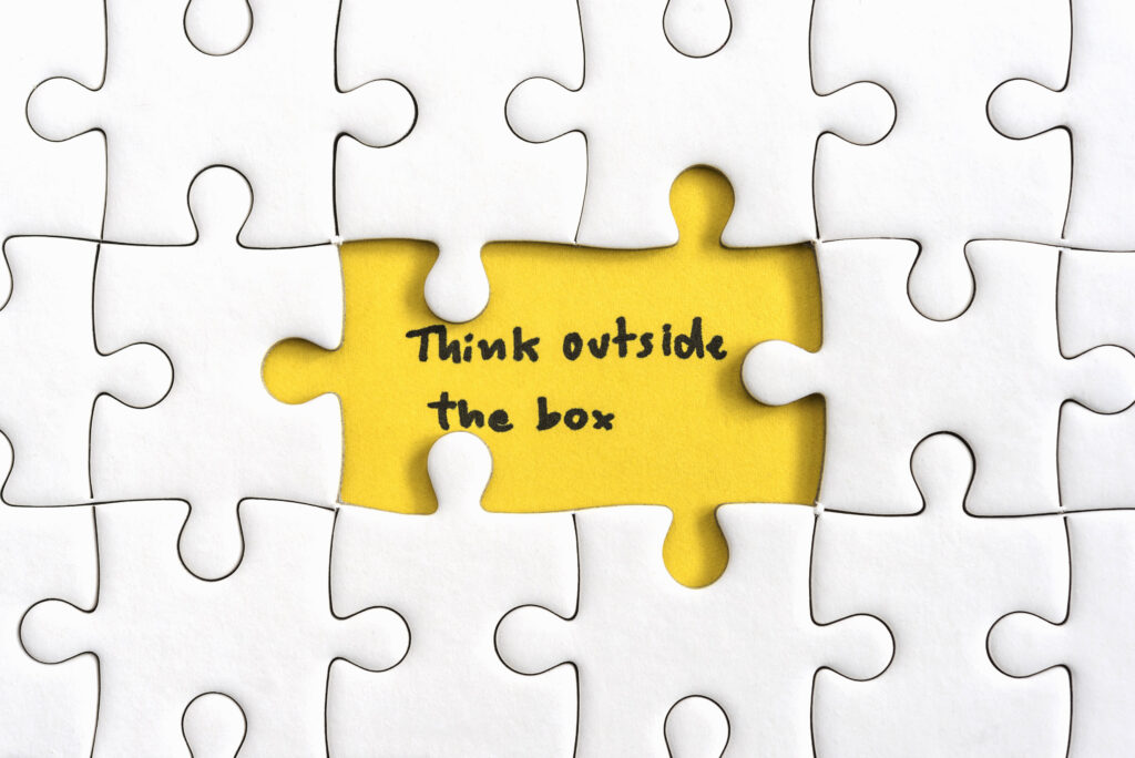 Un rompecabezas blanco al que le falta una pieza que revela una capa amarilla debajo, donde está escrito "pensar fuera de la caja".